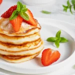 Fluffy mini pancakes stacked with fresh fruit and syrup.