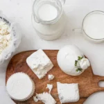Fresh mozzarella cheese being stretched by hand over a wooden countertop.