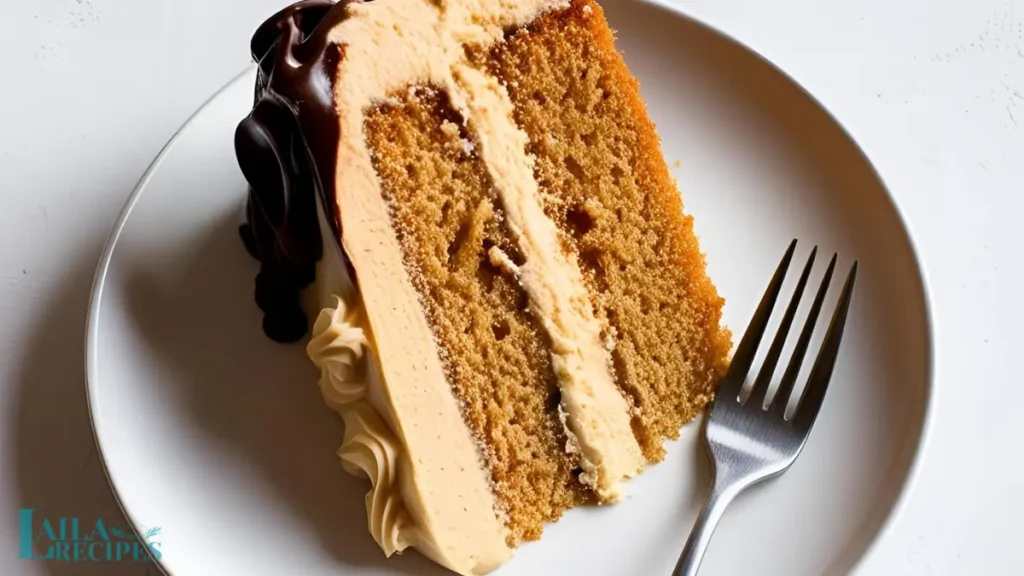Moist peanut butter cake slice topped with creamy frosting and chocolate ganache on a white plate.